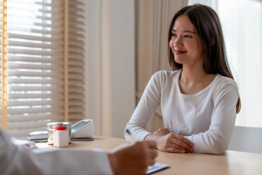 A young woman smiles while talking to a doctor at a desk