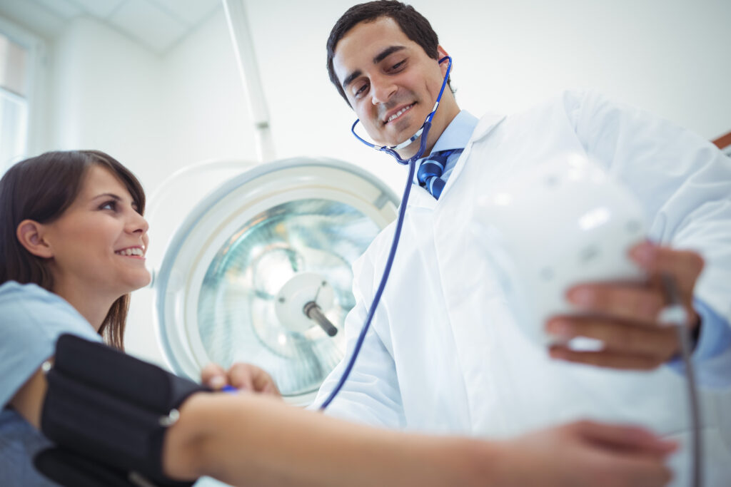 A doctor checks a patient’s blood pressure with a smile.