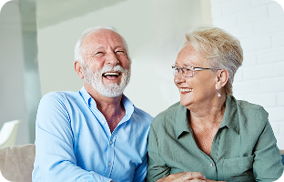 An elderly couple laughing together on a couch.