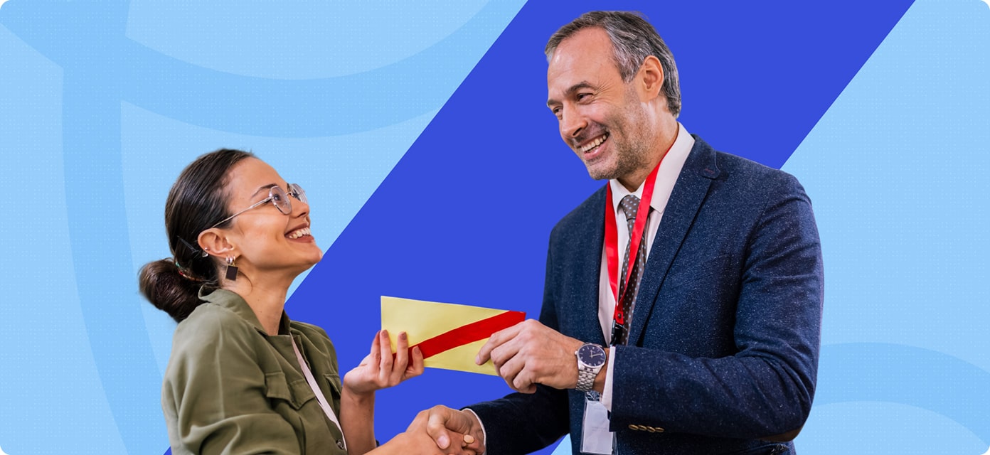 A smiling woman receives an envelope and handshake from a man in a suit.
