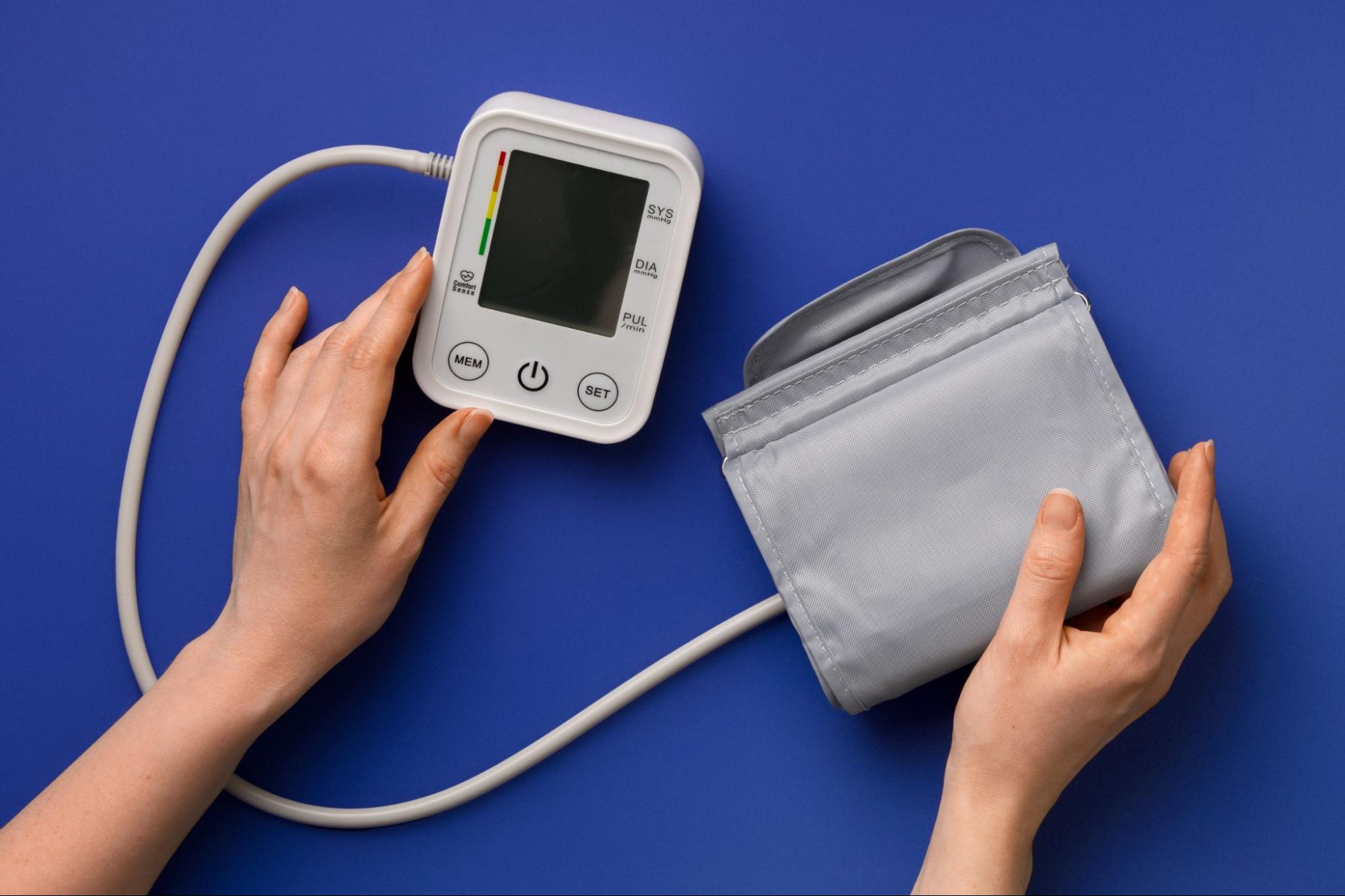 Hands holding a digital blood pressure monitor and arm cuff against a blue background, representing the free medical devices available to NALC Health Benefit Plan members.