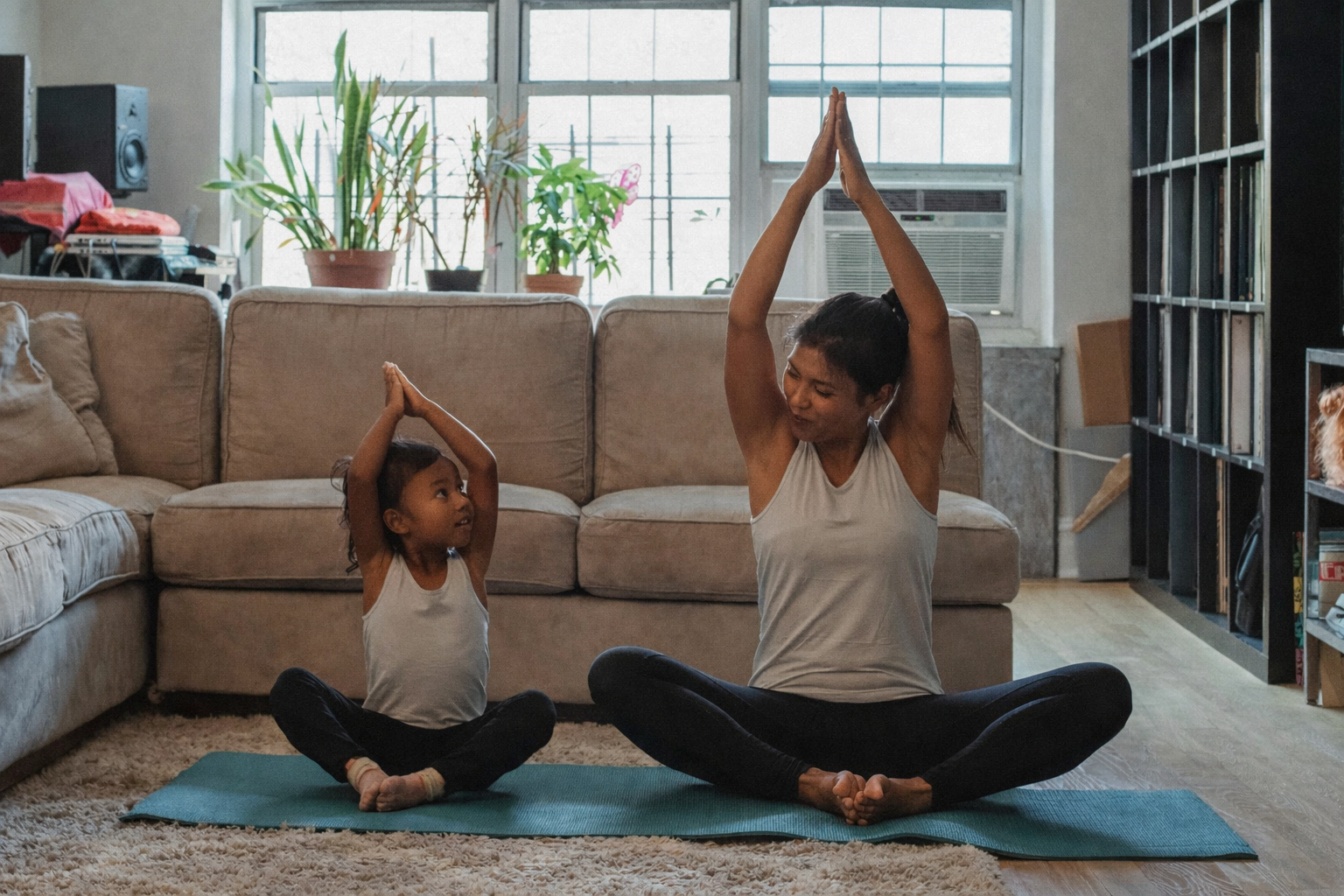 Woman and child sitting on yoga mats raising their arms in a shared yoga pose.